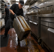 Commercial kitchen worker struggling with heavy oil container